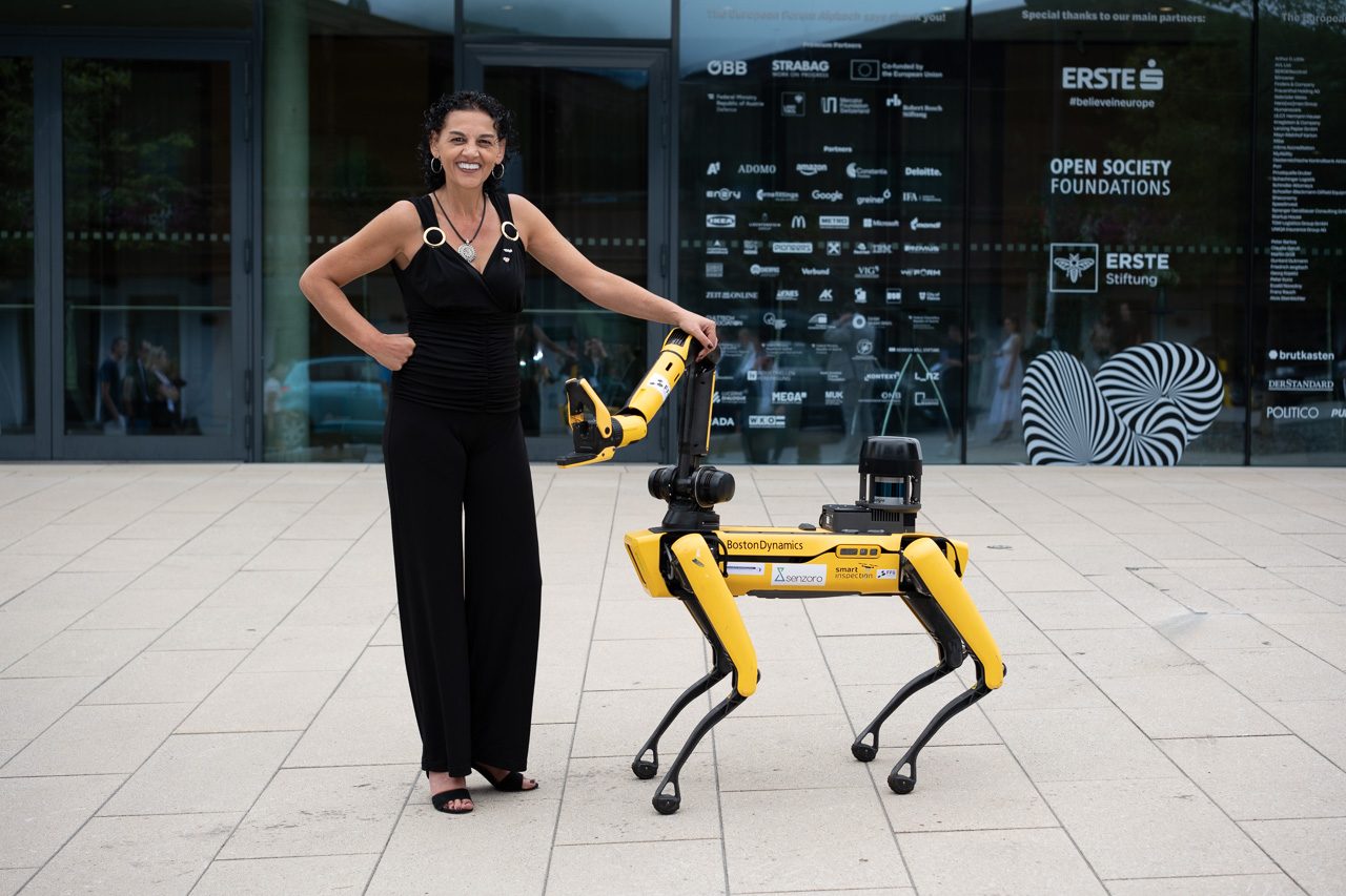 Sabine Singer on stage, with a four-legged robot behind her